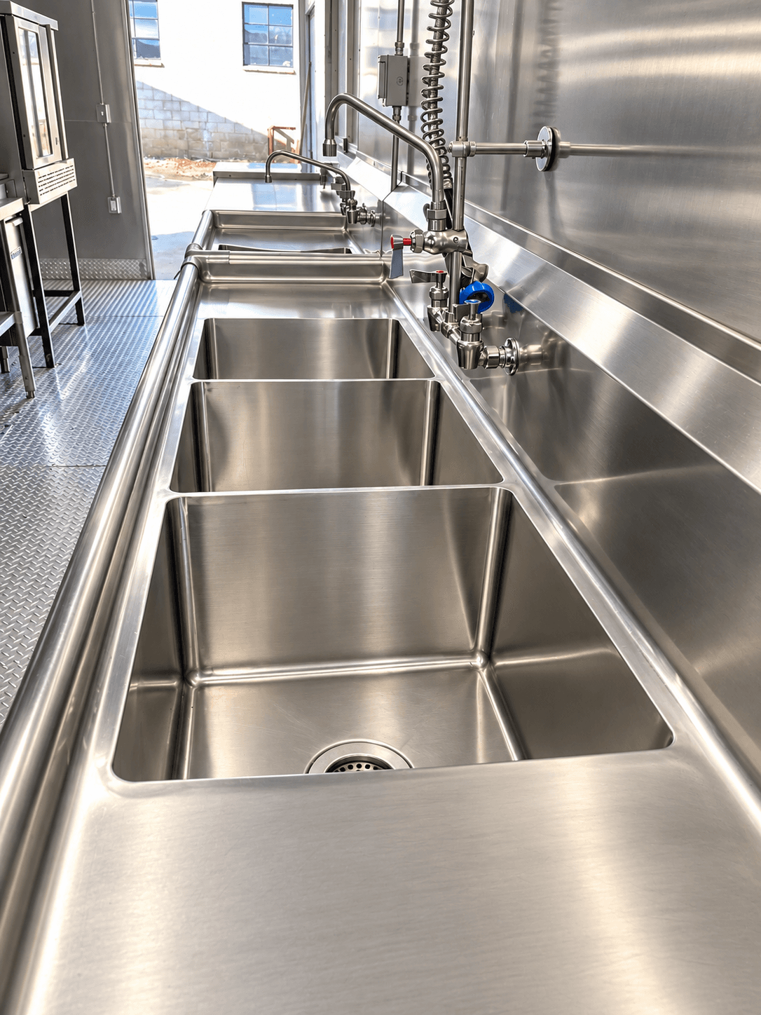 Compartment sinks and stainless preparation surfaces along a kitchen trailer aisle