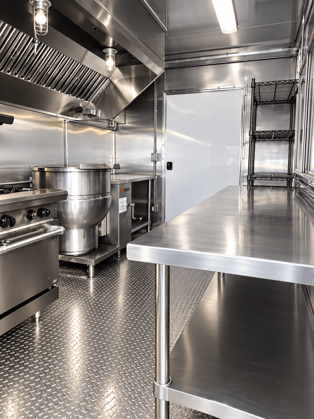 Steam kettle beside stainless preparation surfaces inside a kitchen trailer